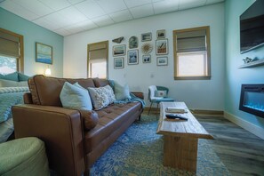 Ein Wohnzimmer mit braunem Ledersofa, einem Holztisch, einem gemusterten Teppich und einer Wand mit gerahmten Bildern.