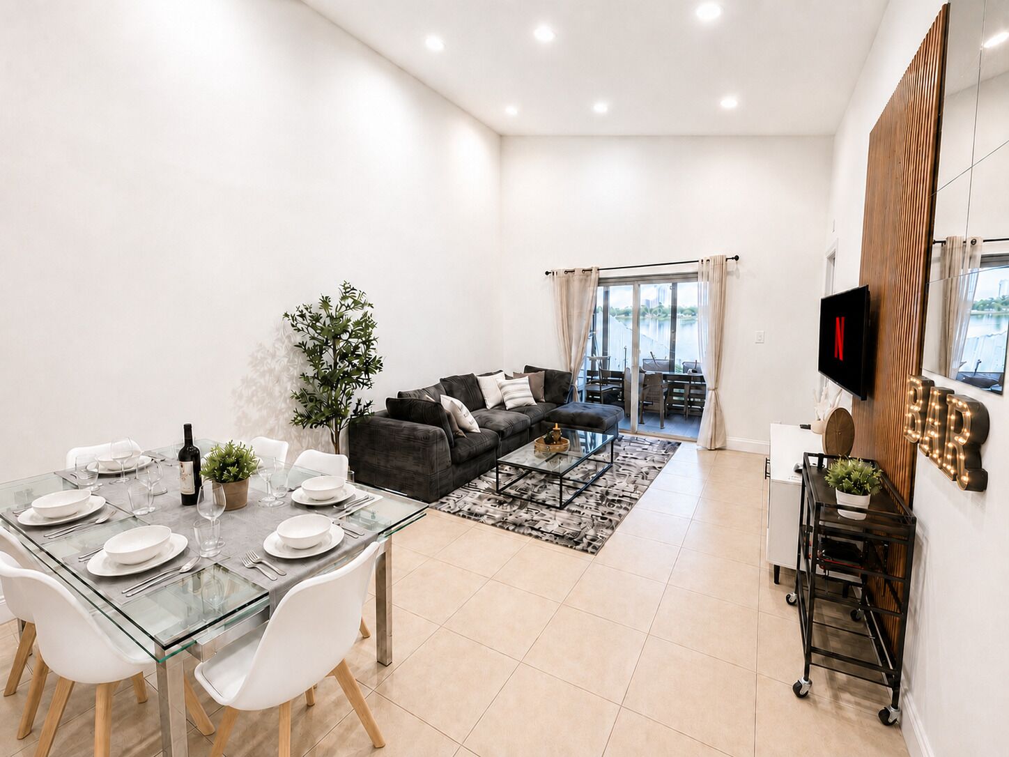 A modern living room with a glass dining table, a sofa, and a TV mounted on the wall.