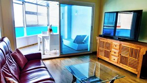 Una sala de estar con un sofá rojo, una mesa de centro de cristal, un aparador de madera y un televisor.