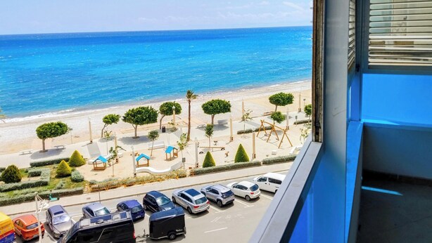 Vista de una playa con coches aparcados, cielo despejado y el océano.
