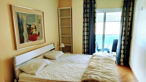 Una cama bien hecha con cabecera, una mesita de noche, una lámpara, una estantería y un cuadro en la pared.