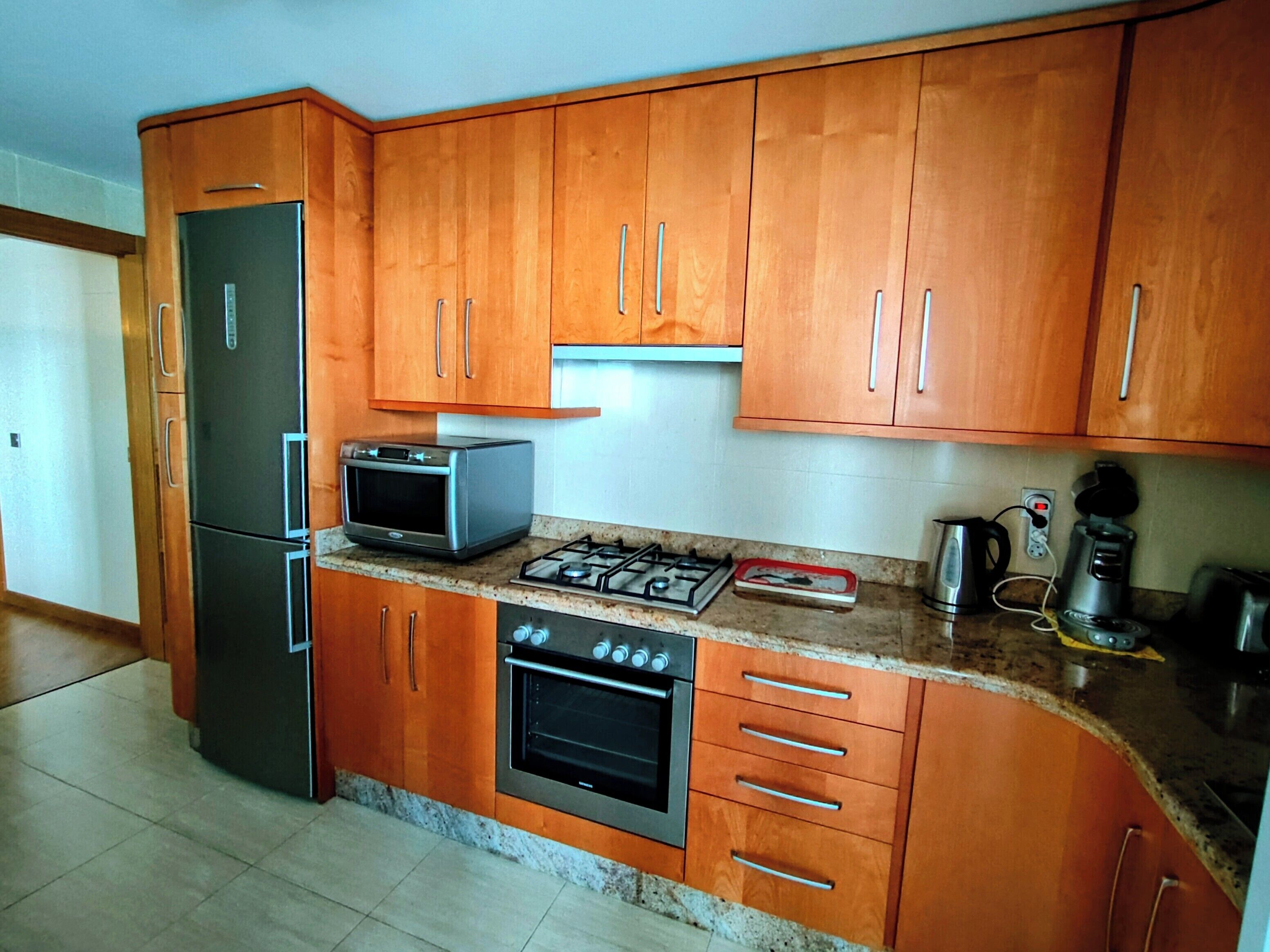 A kitchen with wooden cabinets, a refrigerator, a microwave, a stove, and a coffee maker.