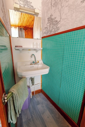 Un baño con lavamanos, espejo y paredes de azulejos verdes.