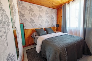 Un dormitorio con cama, mesita de noche, lámpara y ventana con cortinas.