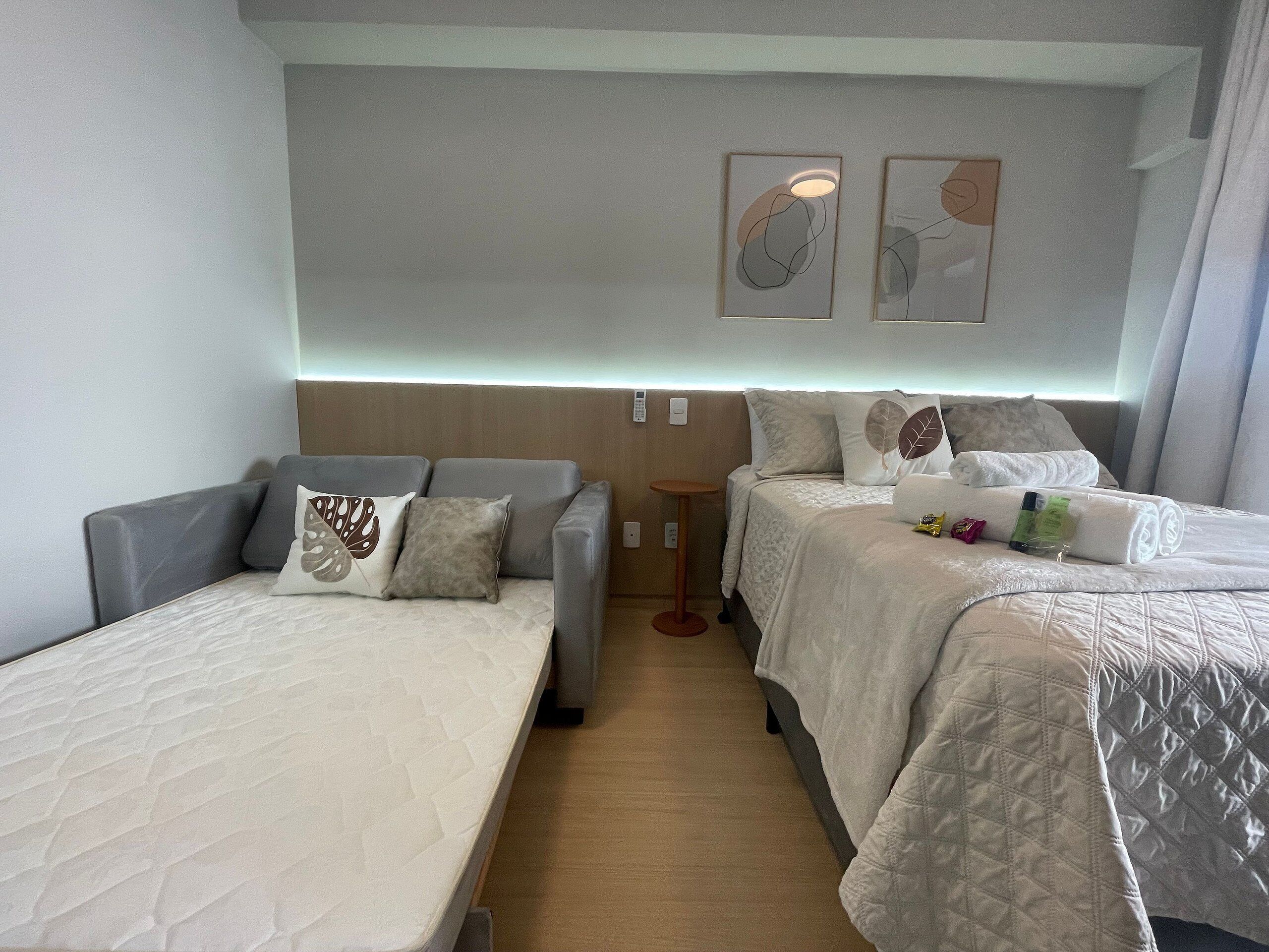 A hotel room with two beds, a sofa, a small table, and artwork on the wall.