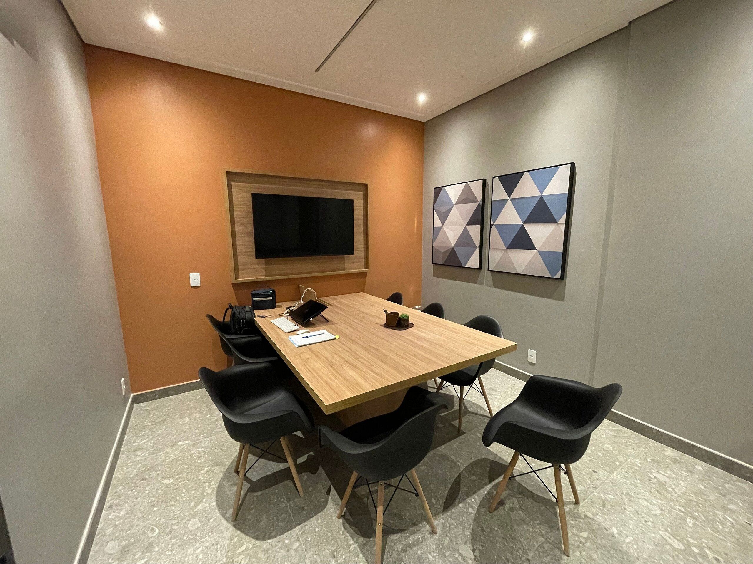 A conference room with a wooden table, black chairs, a TV, and geometric wall art.