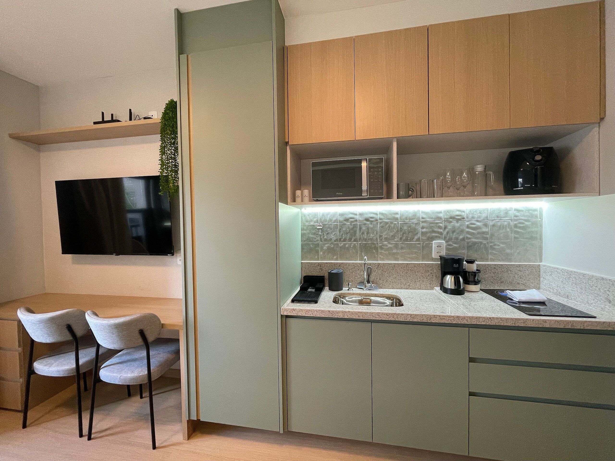 Eine moderne Küche mit Flachbildfernseher, Mikrowelle und Kaffeemaschine. Zwei Stühle und ein kleiner Esstisch sind vorhanden.