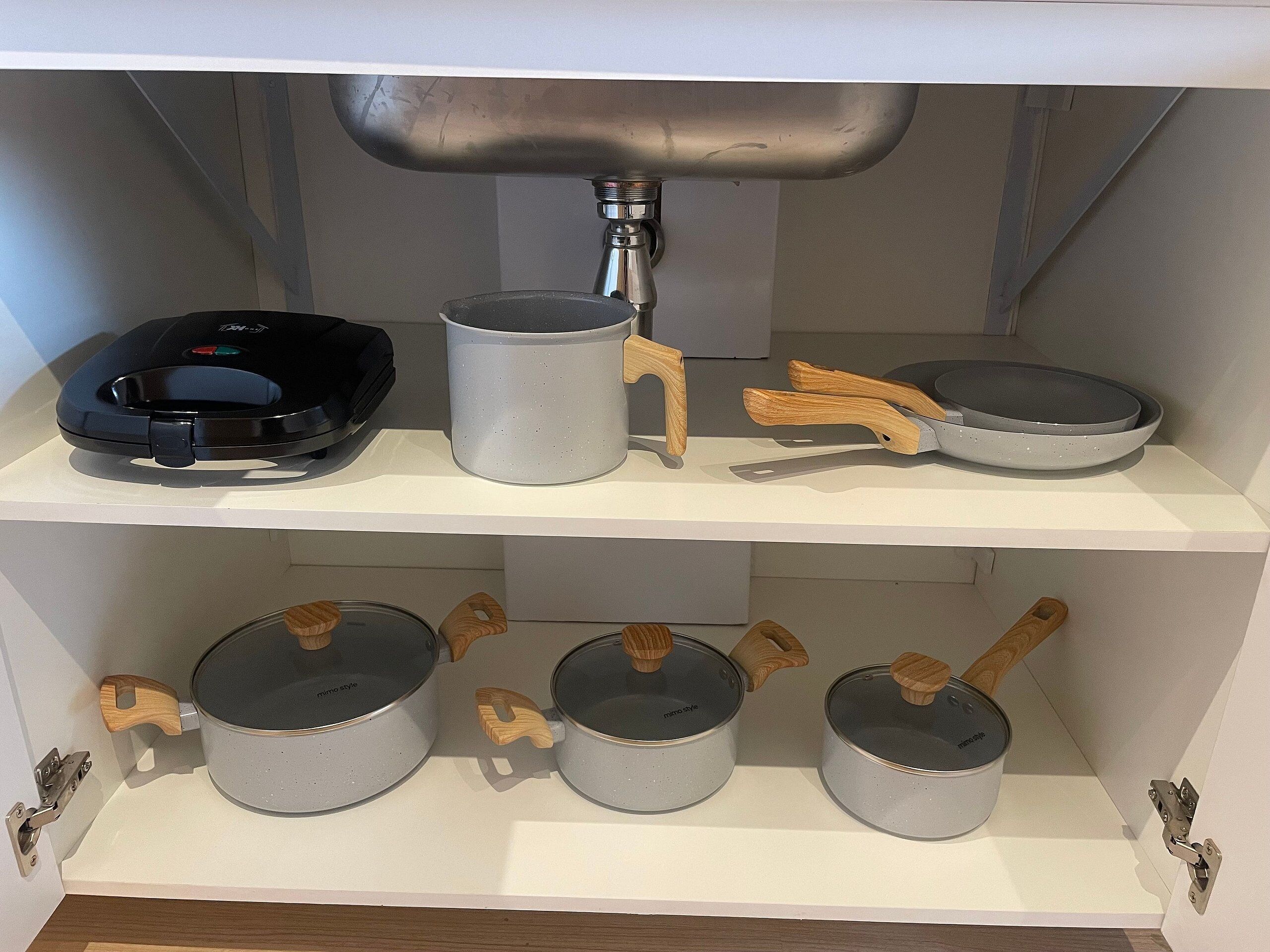 Een keukenschap met een koffiezetapparaat, een waterkoker, een koekenpan en drie pannen.