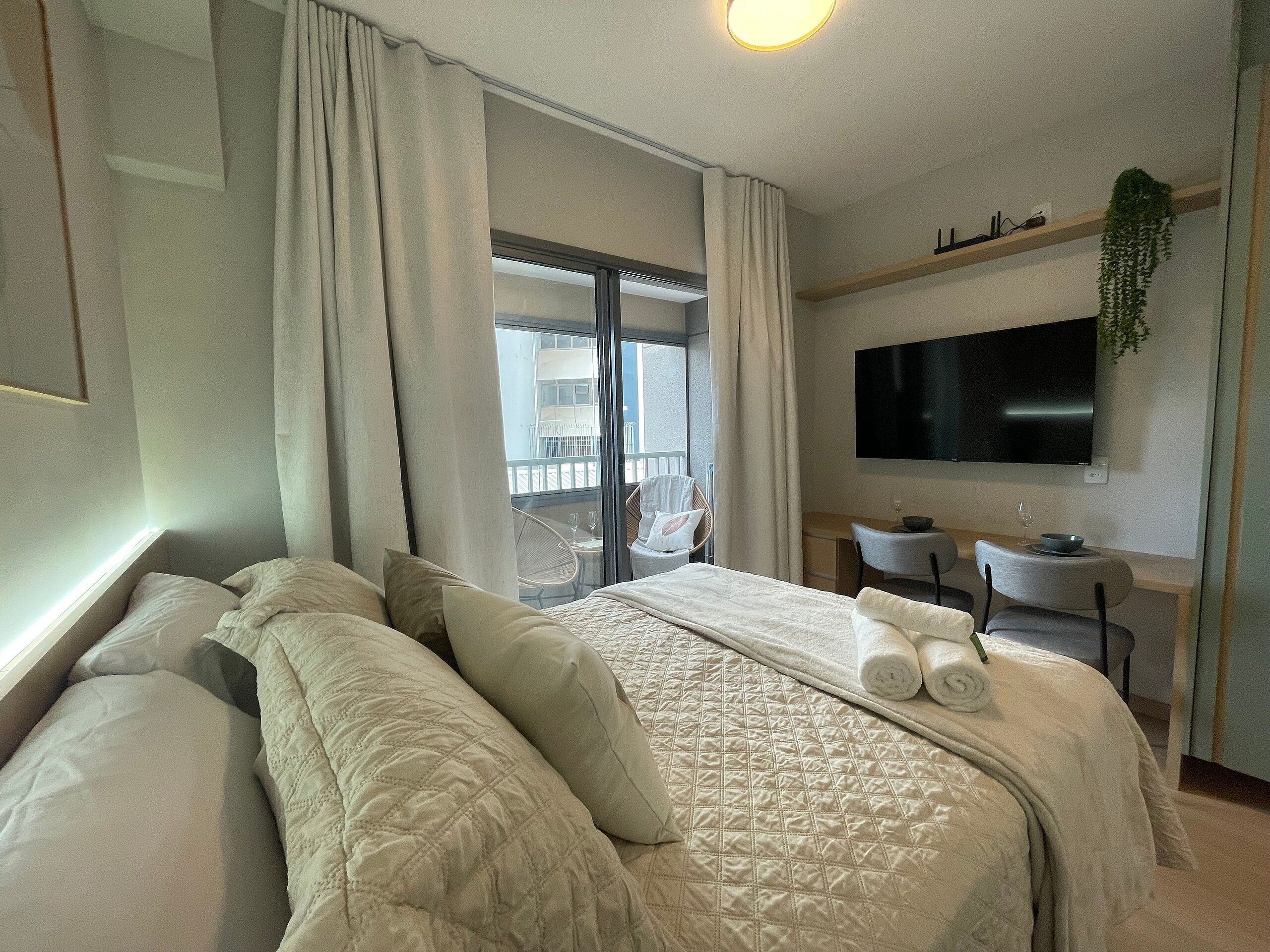 Een hotelkamer met een groot bed, een bureau, een stoel, een televisie en een balkon met een stoel.
