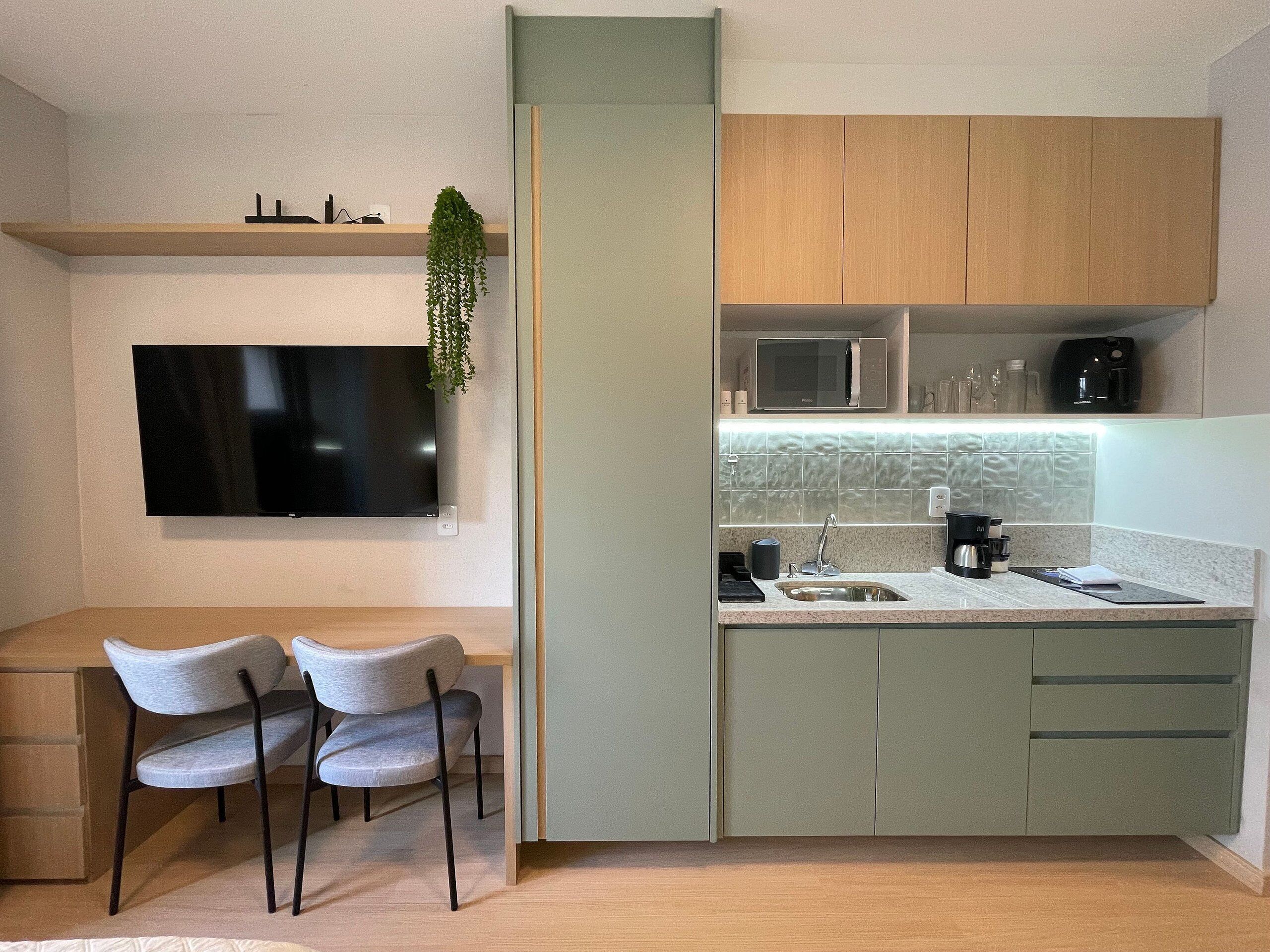 Cocina compacta con televisor de pantalla plana, dos sillas, microondas y cafetera.