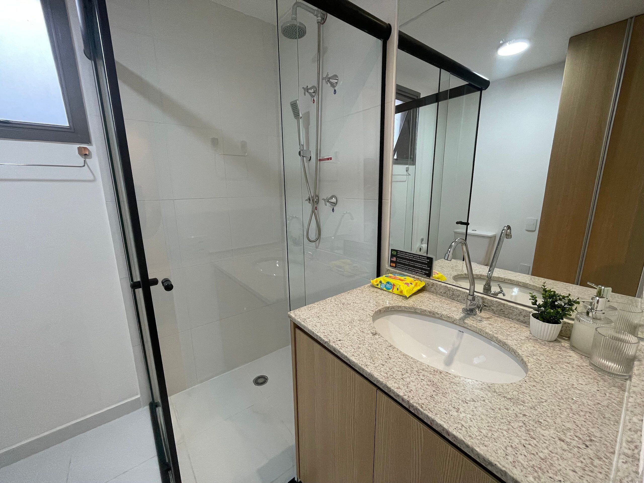 A modern bathroom with a glass shower enclosure, a sink with a granite countertop, and a mirror with a wooden cabinet below.