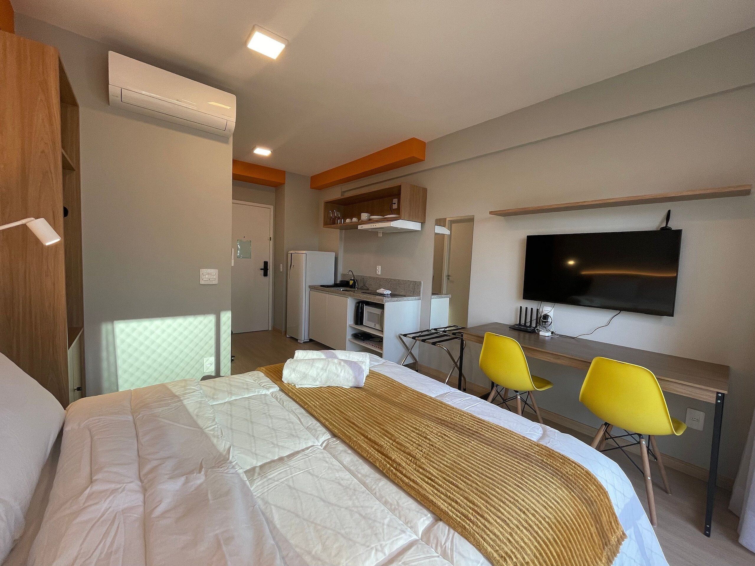 A hotel room with a bed, a desk with two chairs, a TV, and a kitchenette.