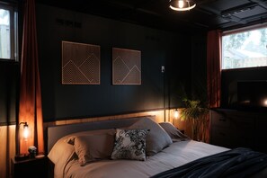 Ein Schlafzimmer mit Bett, Nachttisch, Lampe, Wandbild und Fernseher.