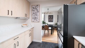 A modern kitchen with light wood cabinets, a marble countertop, a black refrigerator, and a dining area with a wooden table and chairs. - Gateway to the Gorge (Portland)