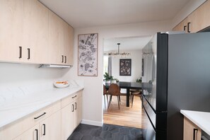 Eine moderne Küche mit hellen Holzschränken, einer Marmorarbeitsplatte, einem schwarzen Kühlschrank und einem Essbereich mit einem Holztisch und Stühlen.