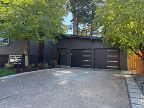 Ein modernes, zweistöckiges Haus mit Auffahrt, Garage und umliegender Bepflanzung.