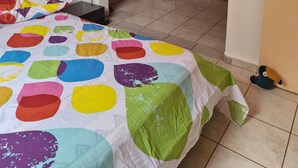 A bedroom with a colorful bedspread, a black headboard, and a view of a balcony with curtains. - House with 3 air-conditioned bedrooms. (Lamentin)