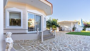 Una casa amb façana corbada, grans finestres, un pati de pedra i mobles d'exterior.