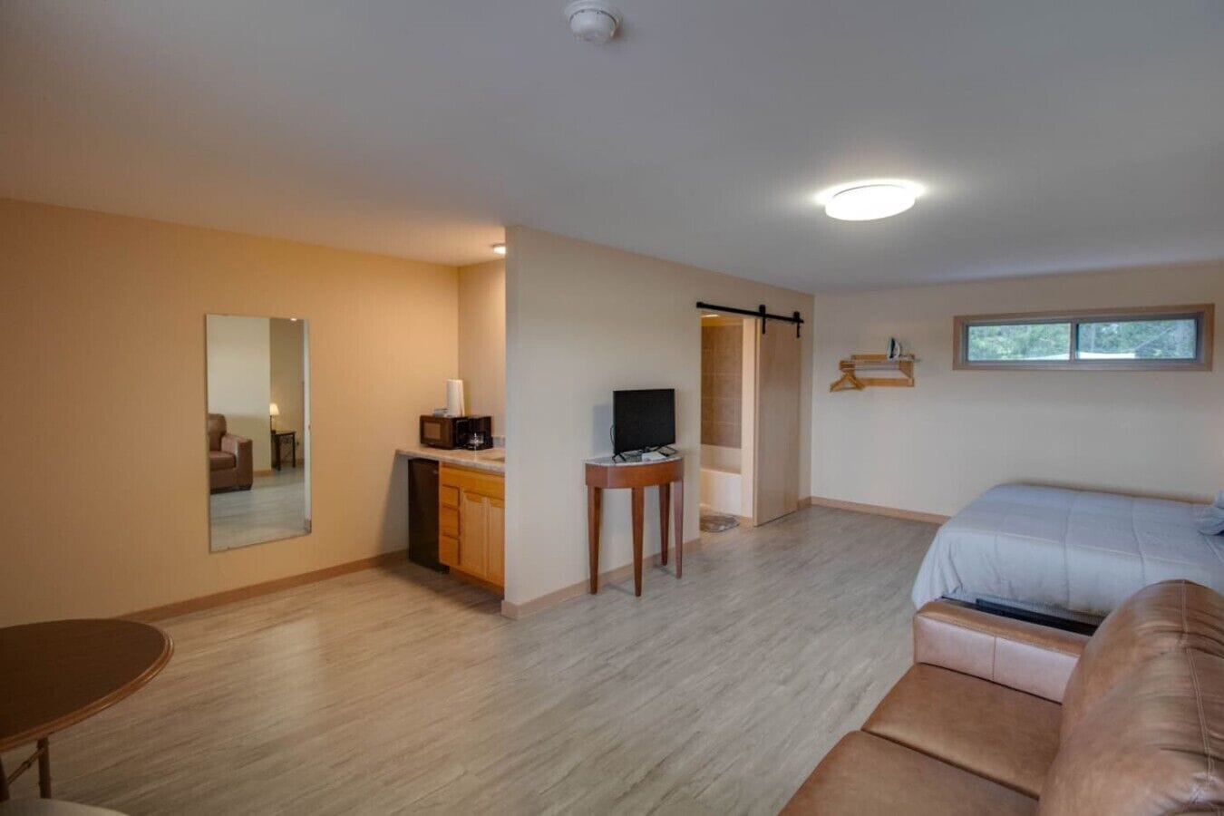 A room with a bed, a small table, a mirror, a TV, and a sliding door leading to a bathroom.