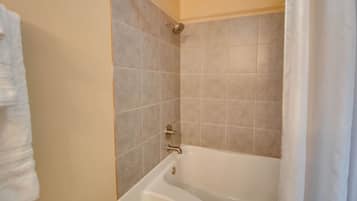 Een badkamer met een bad, betegelde wanden en een douchekop.