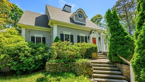 A two-story house with a stone staircase leading to the front door, surrounded by lush greenery and a well-maintained lawn. - Luxury Lake Front w/ Grill and Fire Pit - Perfect for Autumn Retreat (Yarmouth)