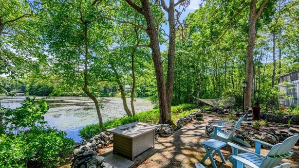 A serene outdoor seating area with Adirondack chairs, a fire pit, and a pond. - Luxury Lake Front w/ Grill and Fire Pit - Perfect for Autumn Retreat (Yarmouth)