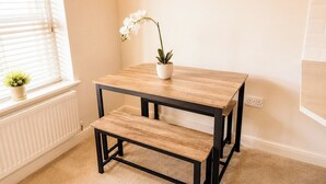 A small, neatly arranged room with a wooden table and bench, a potted plant, and a wall-mounted light fixture. - Modern Apartment in the Heart of Bourne | Sleeps 4 (Bourne)