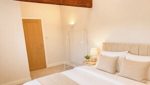 A bedroom with a bed, bedside table, lamp, and a door. - Modern Apartment in the Heart of Bourne | Sleeps 4 (Bourne)