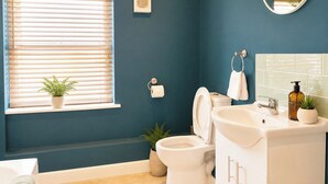 A bathroom with a toilet, sink, mirror, and window with blinds. - Modern Apartment in the Heart of Bourne | Sleeps 4 (Bourne)