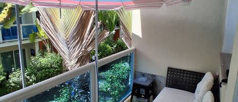 A balcony with a bed, a small table, and a striped umbrella.