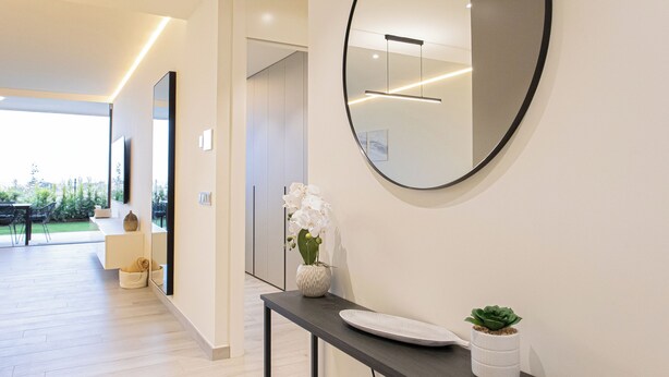 Un couloir moderne agrémenté d’un miroir rond, d’une console et d’une plante en pot.