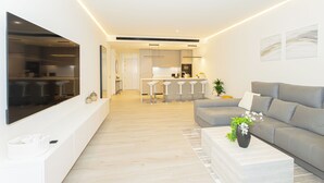 Un salon moderne avec un canapé gris, un téléviseur à écran plat et une cuisine en arrière-plan.