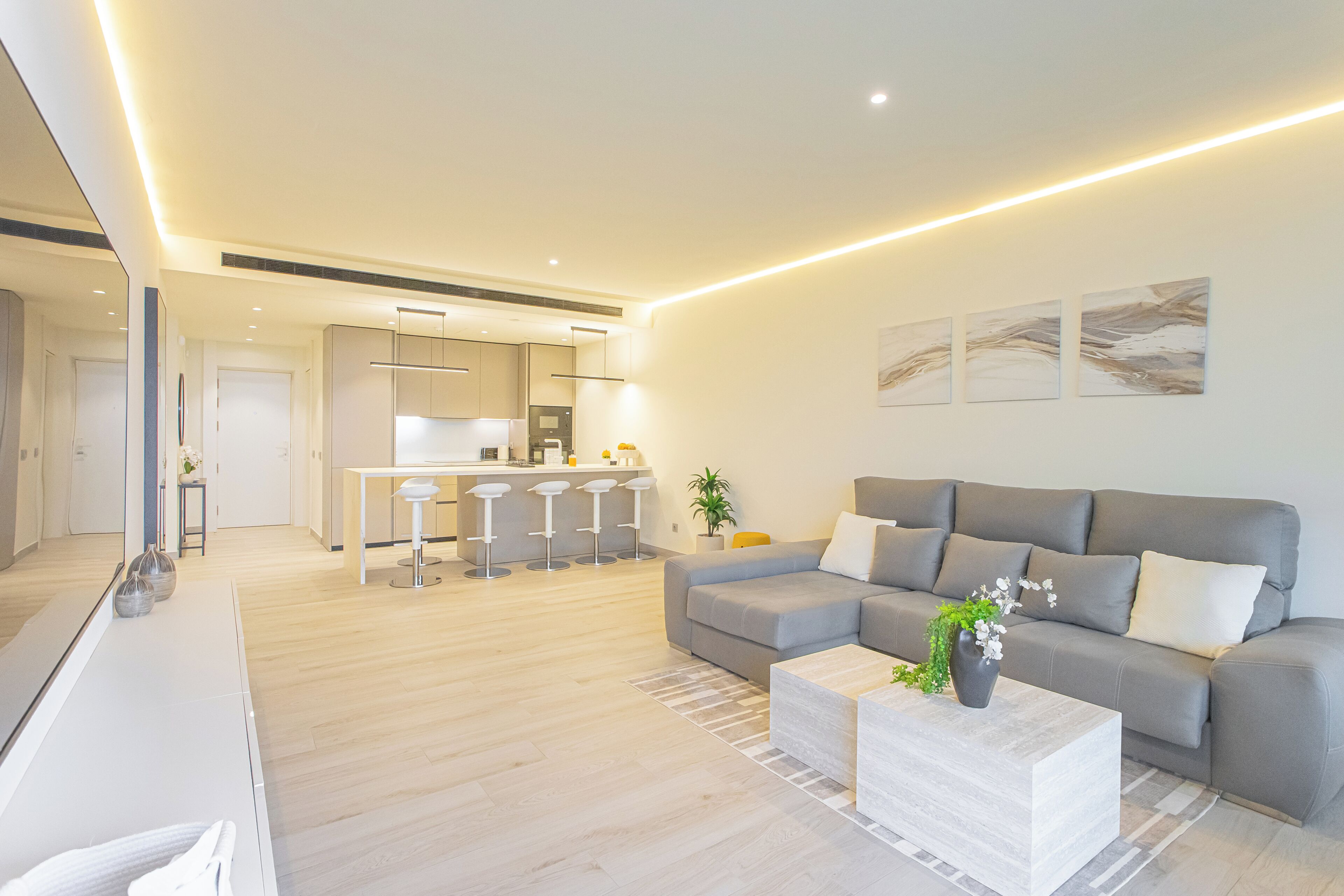 A modern living room with a grey sofa, a coffee table, and a kitchen in the background.