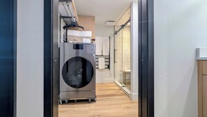 Une buanderie moderne équipée d’un lave-linge à chargement frontal, d’un étendoir et d’une cabine de douche en verre.
