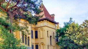 A large, yellow building with a red roof, surrounded by lush greenery and a well-maintained lawn.