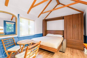 Ein Schlafzimmer mit einem Bett, einem Holzschrank, einem Spiegel, einem Fenster und einem Stuhl.