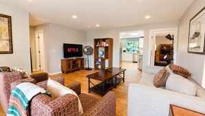 Ein Wohnzimmer mit Fernseher, Ventilator, Bücherregal und Esstisch.