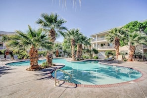 A pool area with palm trees, lounge chairs, and a building with balconies. - Newly updated cozy 2-bedroom condo with spacious balcony (St. George)