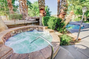 A hot tub surrounded by palm trees and a pool, with a stone border and metal railing. - Newly updated cozy 2-bedroom condo with spacious balcony (St. George)
