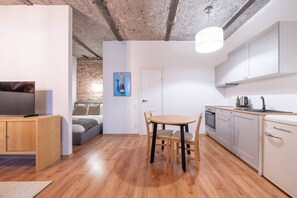 Ein kompakter Wohnraum mit Küchenzeile, einem Essbereich und einem Schlafzimmer mit Backsteinwand.
