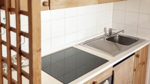 Una cocina con cocina por inducción negra, un lavamanos de acero inoxidable y armarios de madera.