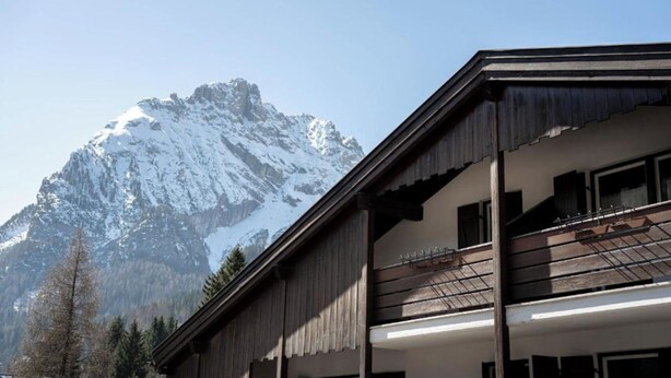 Una cabaña de montaña con fachada de madera y balcones, frente a un paisaje de picos nevados.