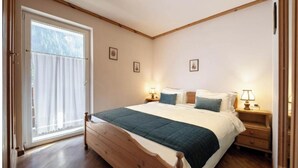 Un dormitorio con una cama de madera, dos mesitas de noche con lámparas, una ventana con persianas y una puerta.