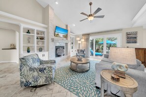 A spacious living room with a fireplace, a ceiling fan, and a view of the outdoors. - 🌴Serenity Cottage | Walk to Beach | Golf Cart (LSV)🌴 (Miramar Beach)