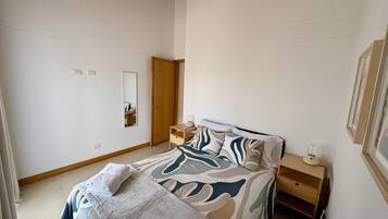 A bedroom with a bed, bedside table, nightstand, mirror, wardrobe, and a framed picture on the wall.