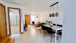 A modern dining area with a glass table, black chairs, and a hanging light fixture.