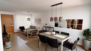 A modern living room with a dining area, a sofa, a coffee table, and a large window with blinds.