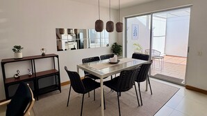 A modern dining area with a glass table, black chairs, a woven pendant light, and a view to the outside.