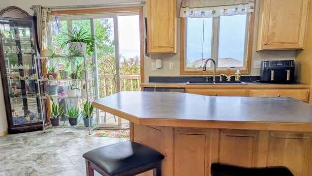 A kitchen with a large island, wooden cabinets, a built-in dishwasher, and a window with a view of greenery.