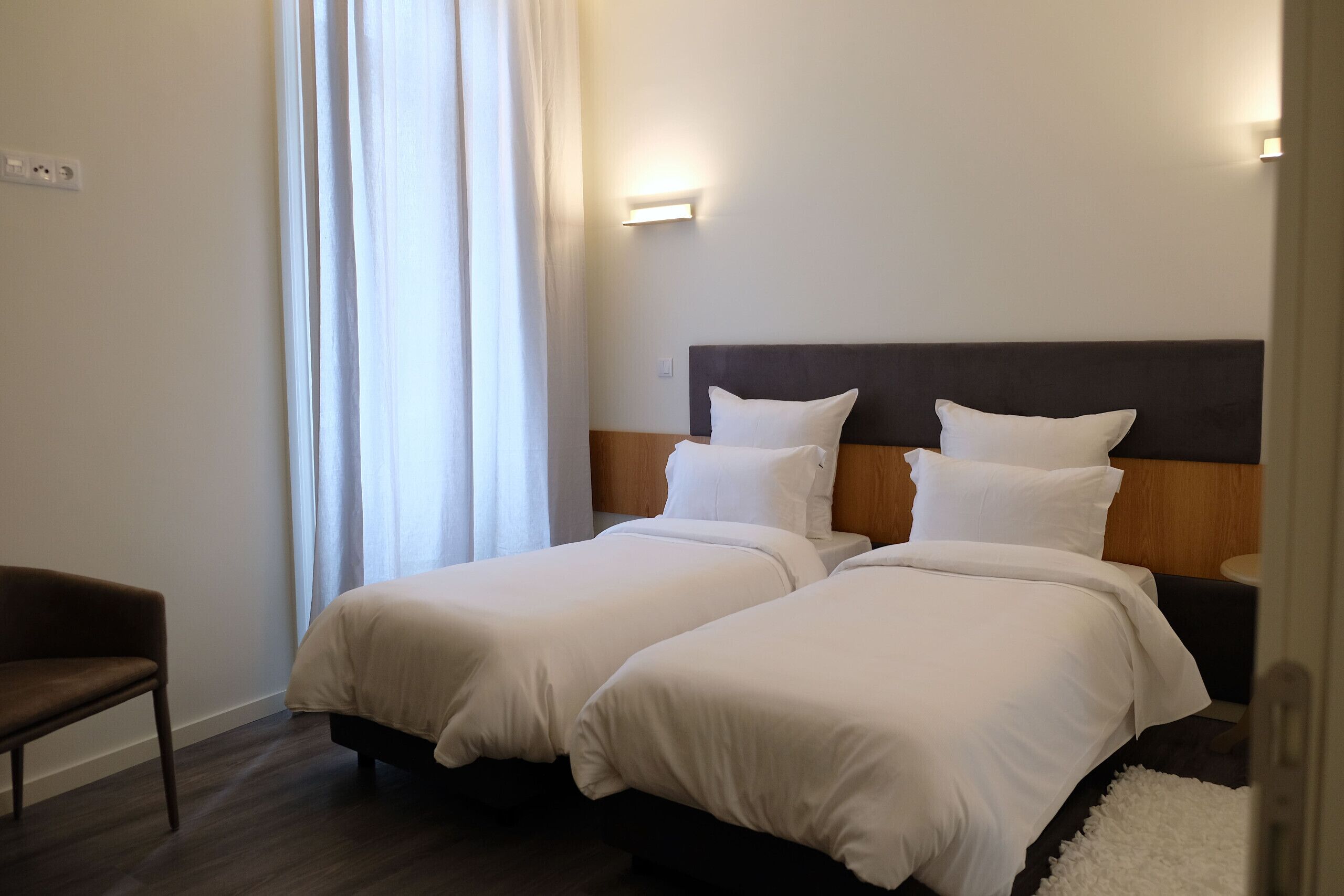 Habitación de hotel con dos camas, una silla, una mesita de noche y una lámpara fijada a la pared.